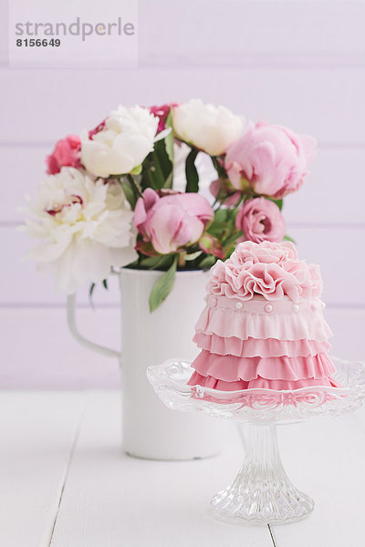 Rosa Mini-Torte mit Blumenstrauß auf dem Tisch  Nahaufnahme