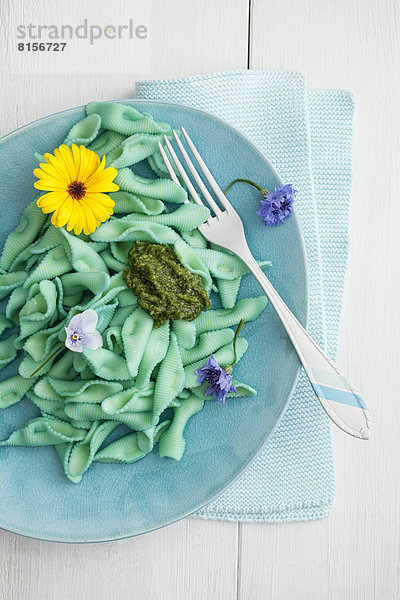 Hausgemachte blaugrüne Pasta mit Basilikum  Pesto und essbaren Blumen auf dem Teller