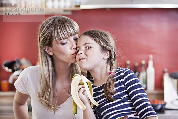 Deutschland  Nordrhein-Westfalen    Mädchen isst Banane während Mutter küsst