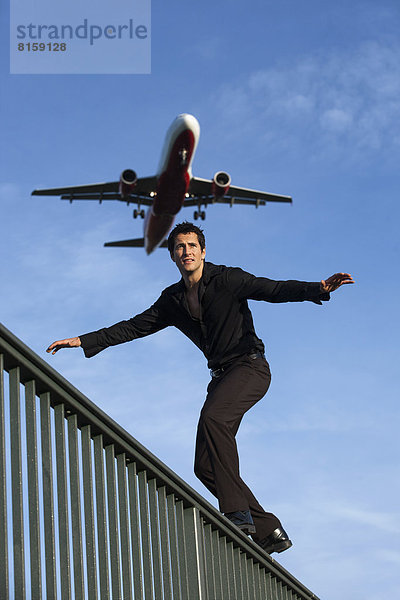 Mittelgroßer Mann am Geländer mit Landeflugzeug im Hintergrund