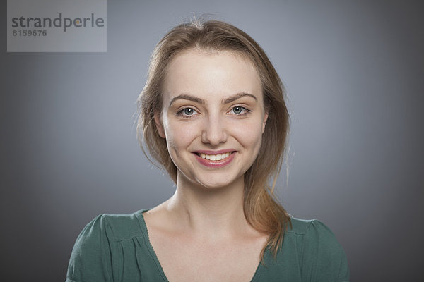 Porträt einer jungen Frau vor grauem Hintergrund  lächelnd