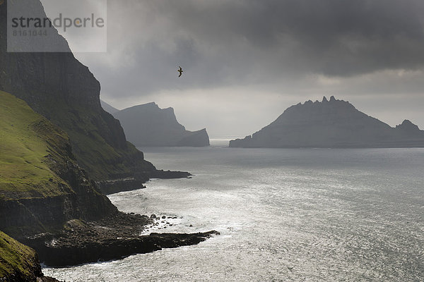 Steilküste  hinten die Silhouette des schroffen Felsens Tindhólmur oder Tindholmur
