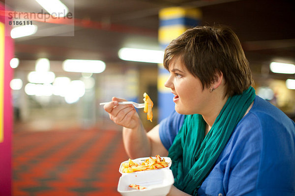 Junge Frau isst Pommes frites zum Mitnehmen