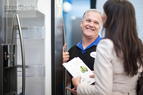 Verkäufer zeigt Frau Kühlschrank im Showroom