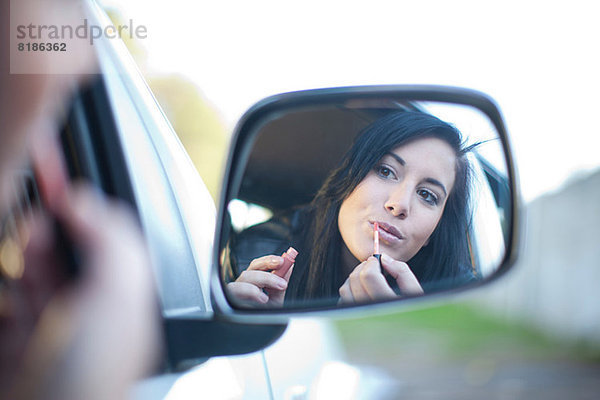 Junge Frau beim Auftragen von Lippenstift im Autospiegel Mund