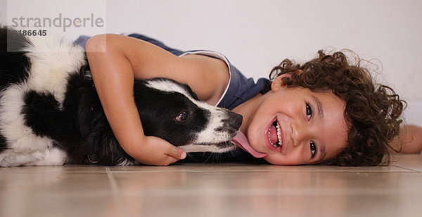 Junge liegt auf dem Boden und umarmt seinen Hund.