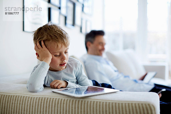 Vater und Sohn sitzen auf dem Sofa mit digitalen Tabletts