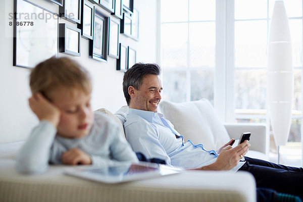Vater und Sohn sitzen auf dem Sofa mit digitalem Tablett und Smartphone