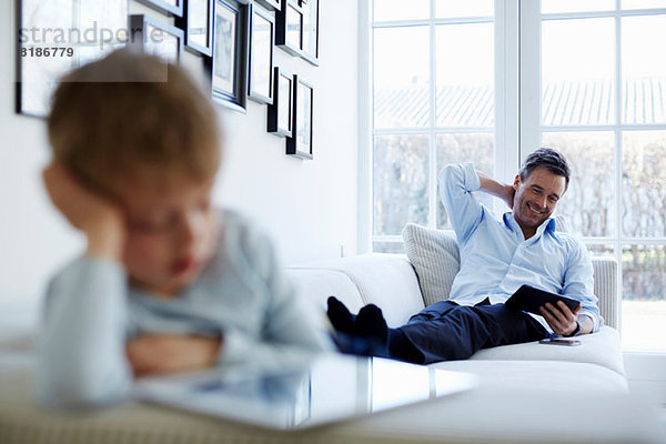 Vater und Sohn sitzen auf dem Sofa mit digitalen Tabletts