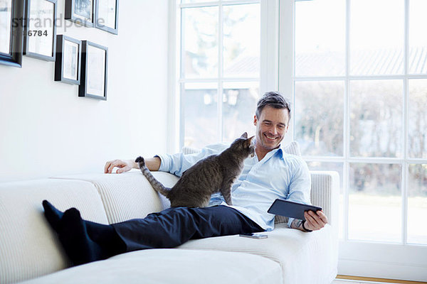 Mann entspannt auf dem Sofa mit digitalem Tablett mit Katze