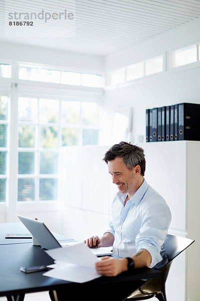 Mann sitzt am Schreibtisch mit Laptop und Papierkram