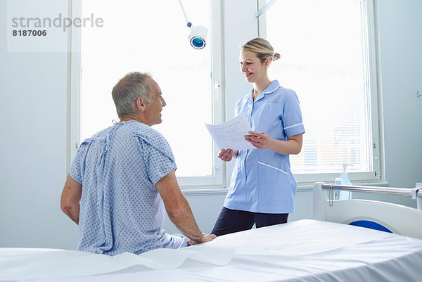 Krankenschwester steht im Gespräch mit Patientin auf dem Krankenhausbett