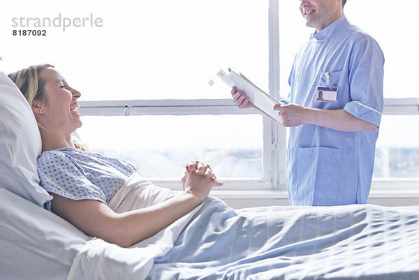 Patientin liegt im Krankenhausbett und lacht mit Krankenschwester