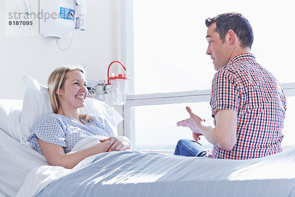 Patient liegt im Krankenhausbett und spricht mit dem Besucher