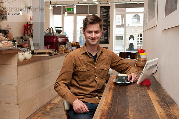 Porträt eines jungen Mannes mit Kaffee und digitalem Tablett im Cafe