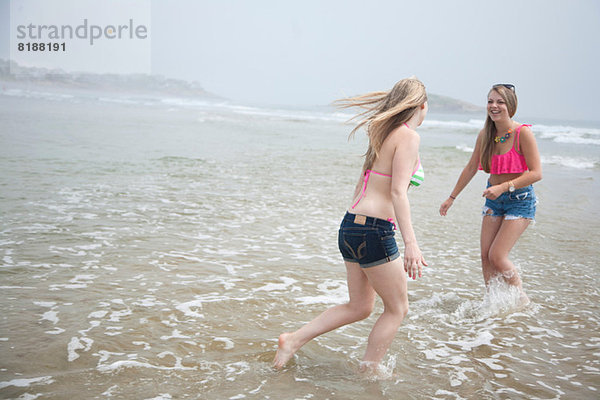 Junge Frauen spielen bei Flut am Strand