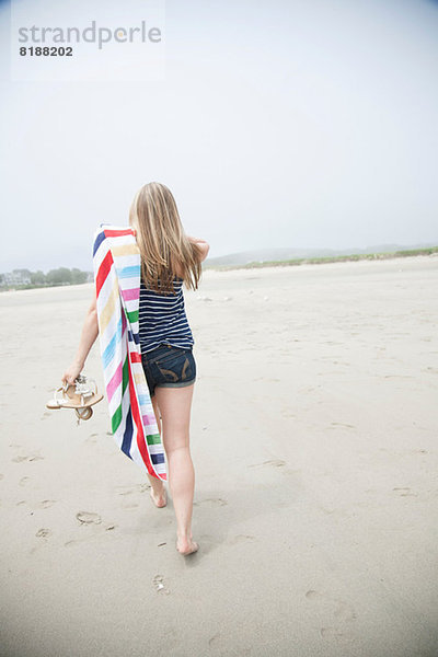 Junge Frau geht mit Handtuch am Strand spazieren