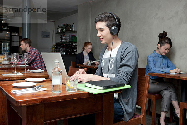 Junger Mann mit Kopfhörer und Laptop im Cafe