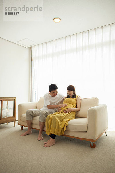 Mann berührt den Bauch einer schwangeren Frau auf dem Sofa