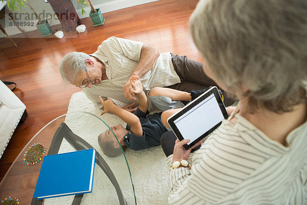 Senior Mann kitzelt Enkel auf dem Teppich