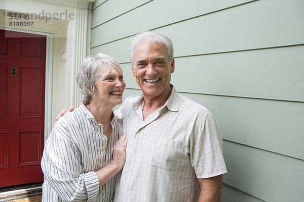 Seniorenpaar lächelt gemeinsam vor dem Haus  Porträt