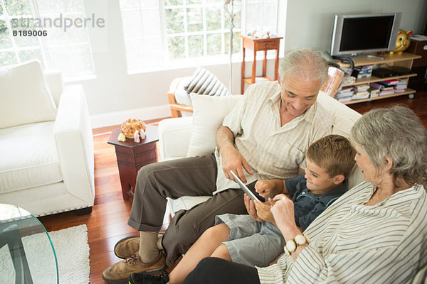 Großeltern sitzend mit Enkel und Blick auf digitales Tablett