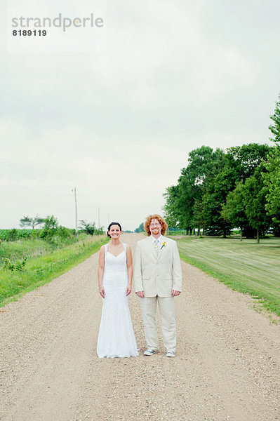 Porträt eines Paares am Hochzeitstag stehend auf einem Feldweg