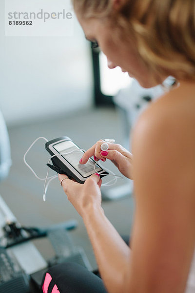 Junge Frau beim Training im Fitnessstudio mit dem Handy