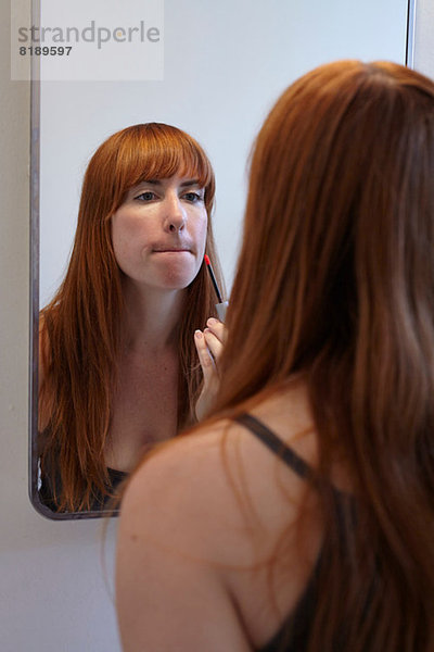 Mittlere erwachsene Frau  die Lipgloss im Spiegel  Mund aufträgt