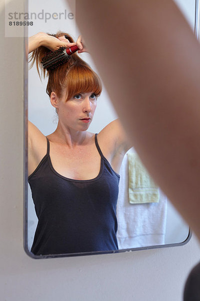 Mittlere erwachsene Frau bürstet Haare im Spiegel