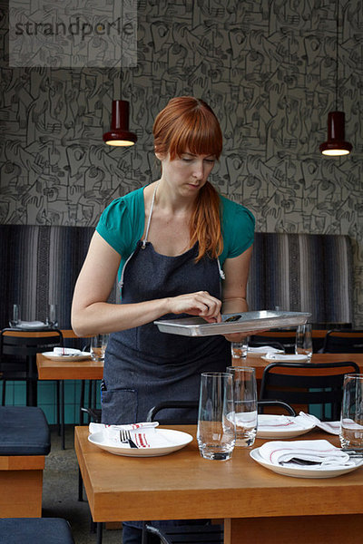 Mittlere erwachsene Frau  die den Tisch im Restaurant zubereitet.