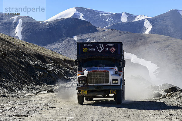 Ein Lkw fährt auf der staubigen kurvenreichen Straße bis zum Gebirgspass Taglang La  5325 m  dem höchsten Pass auf dem Manali-Leh Highway  schneebedeckte Berge hinten
