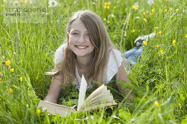 Porträt eines Mädchens auf der Wiese liegend und lesend  lächelnd