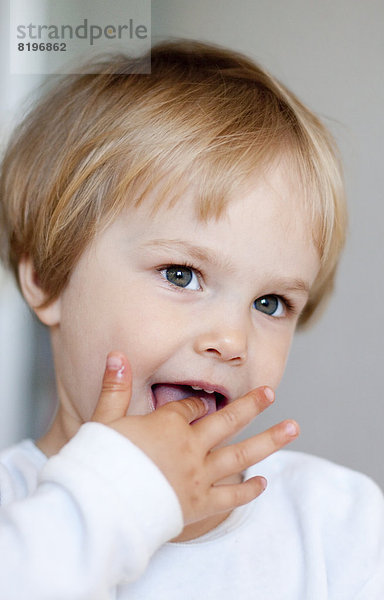 Kleines blondes Mädchen mit dem Finger im Mund