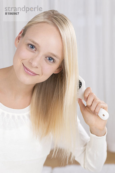 Porträt einer jungen Frau  die sich die Haare bürstet  lächelnd