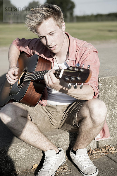 Germany  Young man playing guitar in park