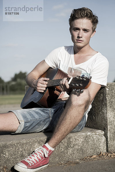 Germany  Young man playing guitar in park
