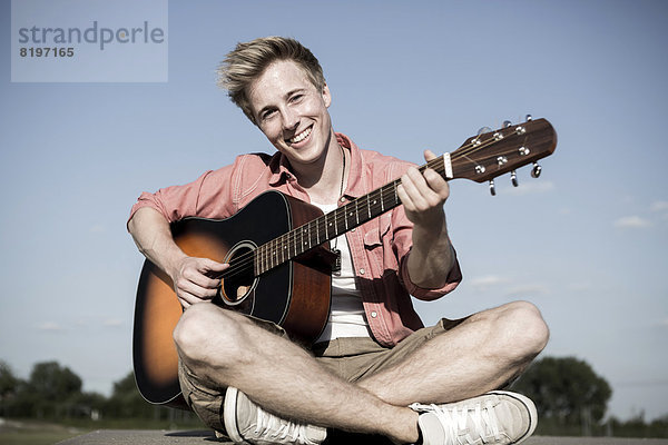 Deutschland  Junger Mann spielt Gitarre im Park