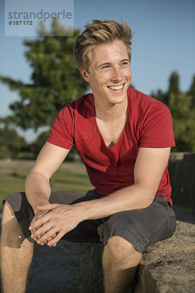 Germany  Young man sitting in park  smiling