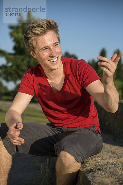 Germany  Young man sitting in park  gesturing