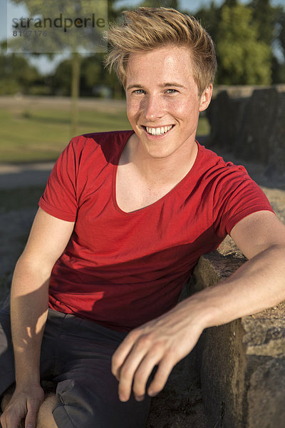 Germany  Young man sitting in park  smiling