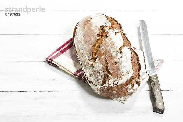 gebackenes Brot mit Serviette und Messer auf Holztisch  Nahaufnahme
