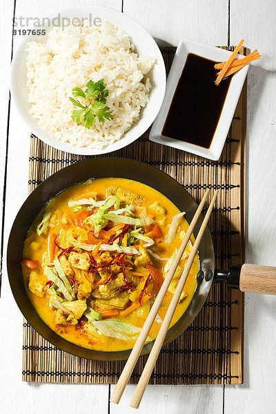 Spicy chicken with red curry  peppers  chillies  carrots  coconut milk and bowl of rice on table mat