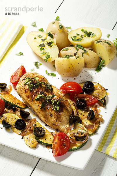 Plate of roasted chicken with potatoes  olives  tomatoes and garnished with herbs on wooden table  close up