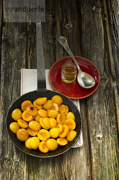 Karamellisierte Aprikosen in der Pfanne mit Ölbehälter und Löffel auf Holztisch  Nahaufnahme