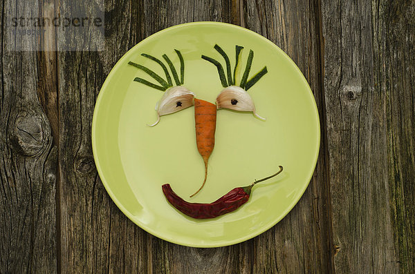 Lustiges Gesicht aus Gemüse auf grünem Teller  Nahaufnahme