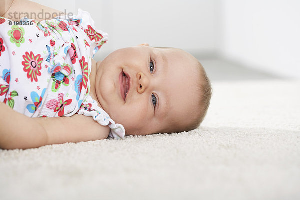 Germany  North Rhine Westphalia    Baby girl lying on carpet  smiling