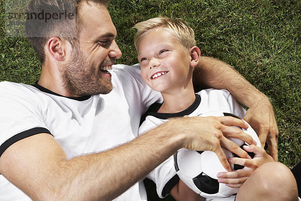 Germany  Father and sun lying on lawn  wearing football shirts