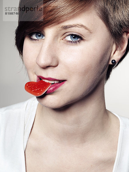 Portrait einer jungen Frau mit Süßigkeitenherz im Mund  Nahaufnahme  Mund