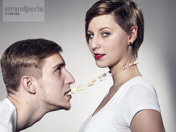 Junger Mann beißt Süßigkeiten Halskette  während die Frau in die Kamera sieht  Mund
